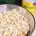 Pipoca Gourmet de Leite Ninho já pronta, em uma bacia de metal com uma lata de leite em pó ao lado