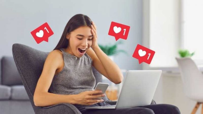 mulher sentada em uma poltrona com o celular e seu notebook, feliz por conseguir seguidores no Instagram grátis
